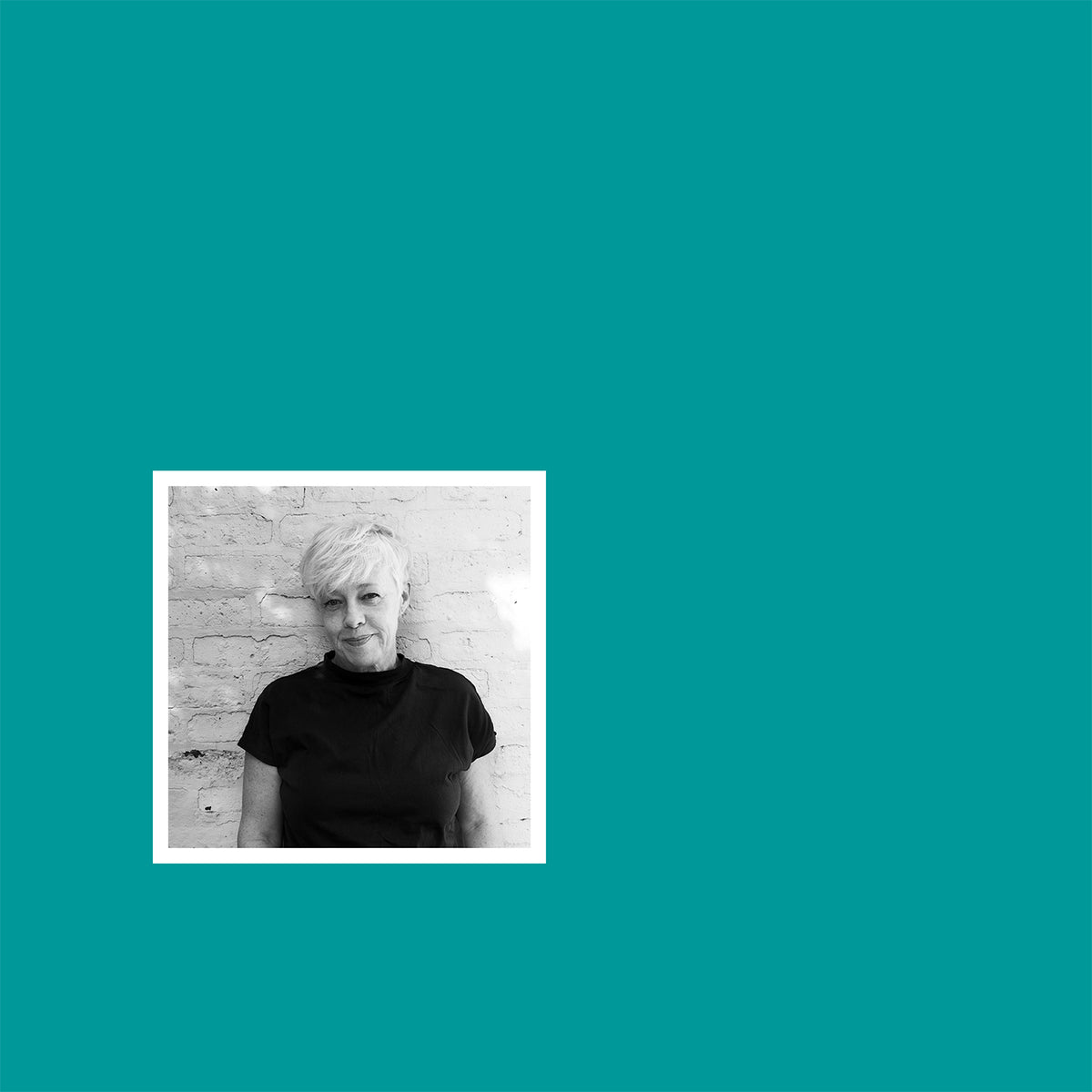 Portrait noir et blanc de la créatrice Laure Vissian devant un mur de briques blanches, encadré sur fond turquoise